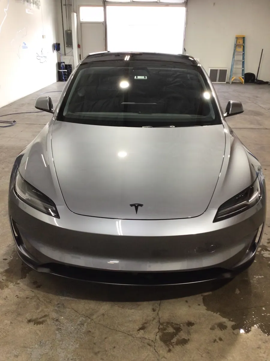 A silver Tesla Model 3 parked nose out on a wet shop floor, freshly washed