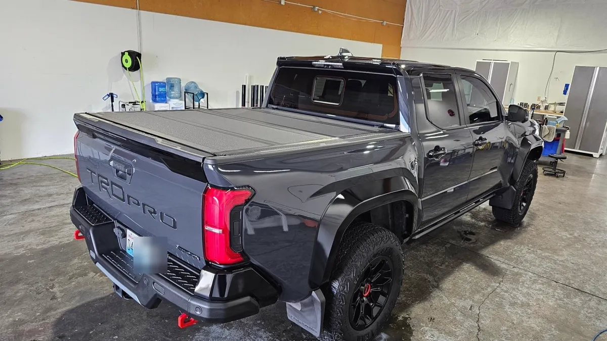 Rear three-quarter view of a dark gray Toyota Tacoma with a bed cover inside the APC shop