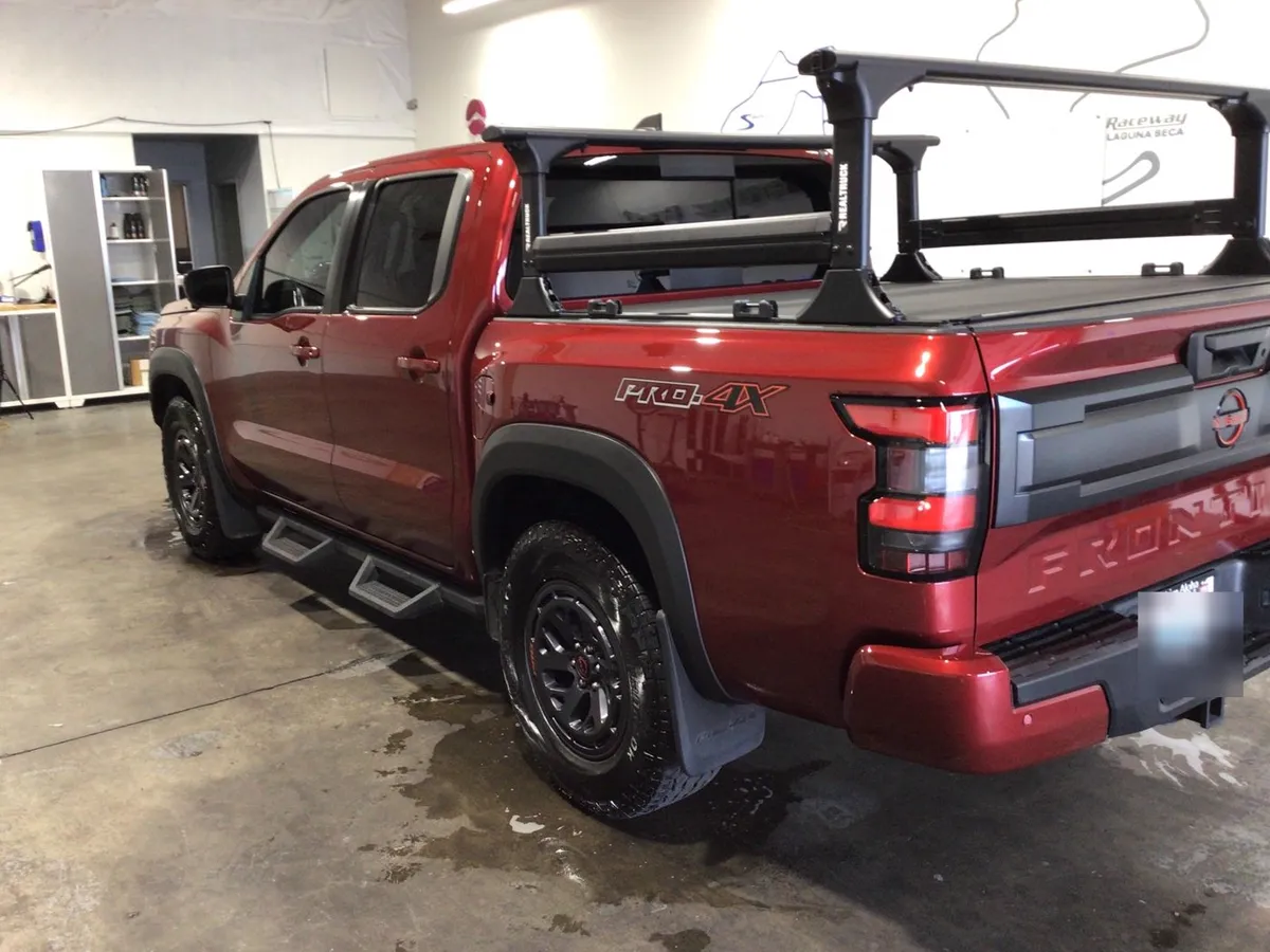 A red Nissan Frontier with a bed rack parked on a wet shop floor
